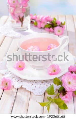 Beautiful fruit blossom with cup of tea on table on light background