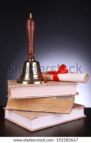 Gold retro school bell with books on table on dark background