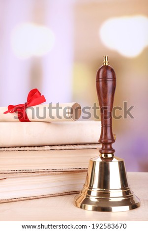 Gold retro school bell with books on table on bright background