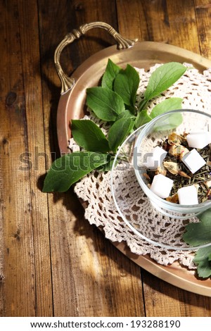 Glass cup with dry flowers and herbs, fruits ingredients for tea, on tray, on color wooden background