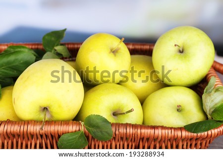 Ripe sweet apples with leaves in wicker basket on light background
