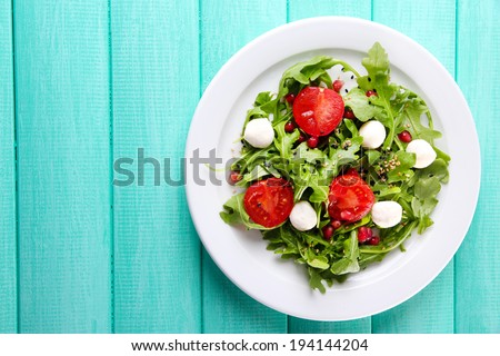 Green salad made with  arugula, tomatoes, cheese mozzarella balls and sesame  on plate, on color wooden background