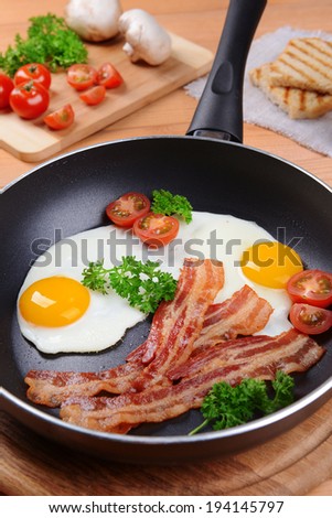 Scrambled eggs and bacon on frying pan on table close-up