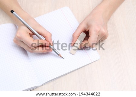 Human hands with pencil writing on paper and erase rubber on wooden table background