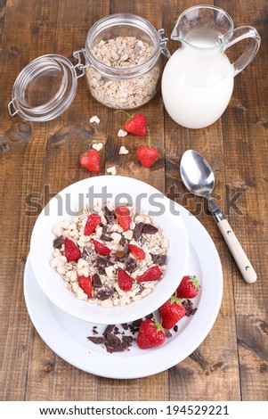 Healthy cereal in bowl with strawberries and chocolate on wooden table