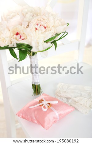 Beautiful wedding bouquet and decorative pillow for wedding rings on chair on light background