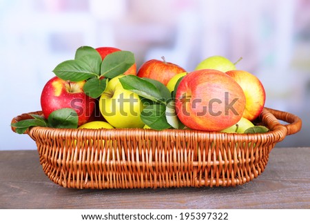 Ripe sweet apples with leaves in wicker basket on light background