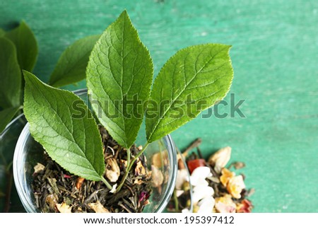 Glass cup with dry flowers and herbs, fruits ingredients for tea, on color wooden background