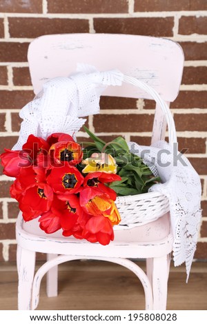 Bouquet of colorful tulips in wicker basket, on chair, on home interior background