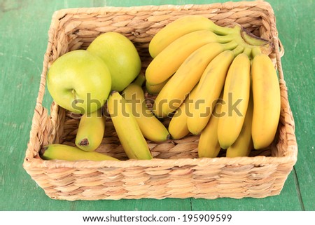 Bunch of mini bananas in wicker box on color wooden background