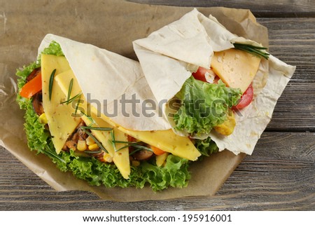 Veggie wrap filled with cheese and fresh vegetables on wooden table, close up