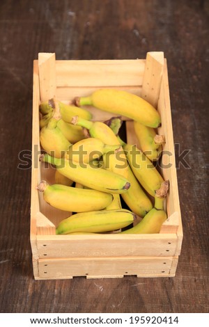 Bunch of mini bananas in wooden box on wooden background