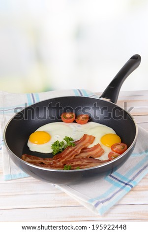 Scrambled eggs and bacon on frying pan on table on light background