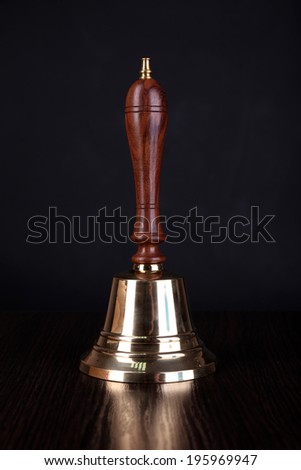 Gold retro school bell on table on black background