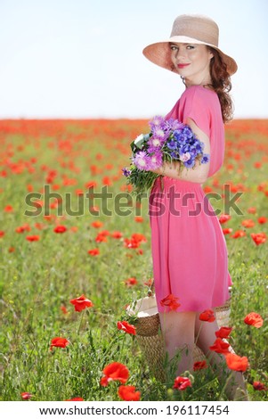Beautiful young woman holding wicker bag in poppy field
