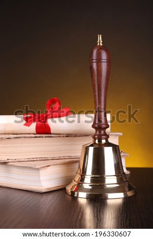 Gold retro school bell with books on table on dark background