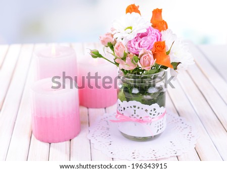 Beautiful bouquet of bright flowers in jar on table on light background