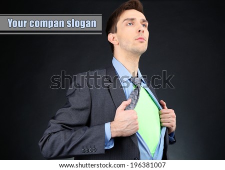 Young business man tearing apart his shirt revealing  superhero suit, on dark background