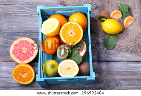 Fresh exotic fruits with green leaves in wooden box on color wooden background