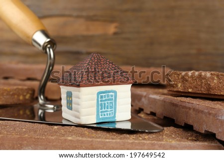 Wooden toy house on trowel and tiles on wooden background, close up