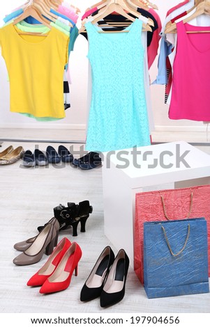 Different clothes on hangers and shoes on light background