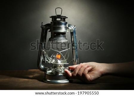 Hand lights a kerosene lamp on dark grey background
