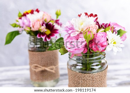 Beautiful bouquet of bright flowers in jars on table on grey background