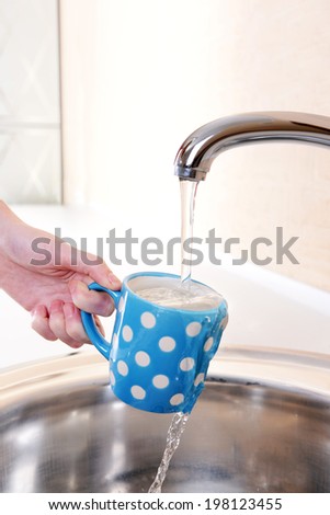 Hand holding  cup of water poured from  kitchen faucet