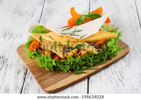 Veggie wrap filled with cheese and fresh vegetables on wooden table