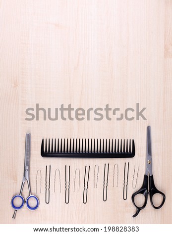 Professional hairdresser tools - comb, scissors and pins on light wooden background