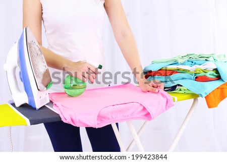 Woman ironing clothes on ironing board, close-up, on light background