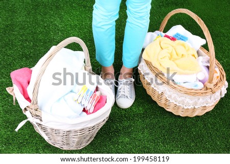 Woman holding laundry baskets with clean clothes, towels and pins, on green grass background