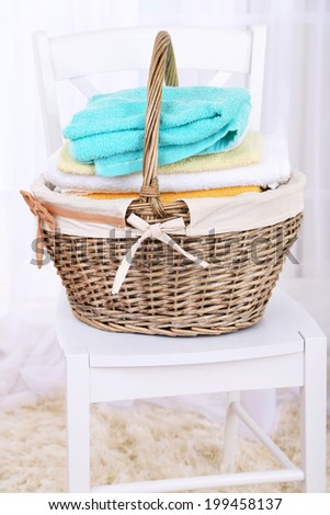 Colorful towels in basket on chair, on light background