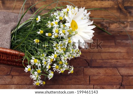 Beautiful bouquet of daisies in wicker basket on wooden background