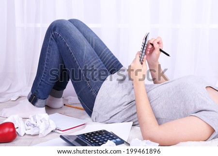 Closeup of young female student lying on floor and studying, on light background