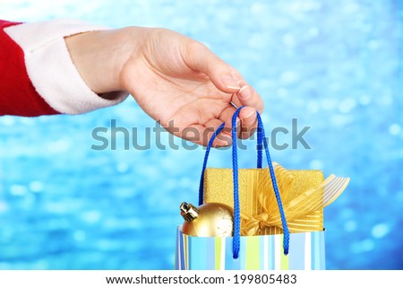 Hand holds package with New Year balls and gifts on blue background