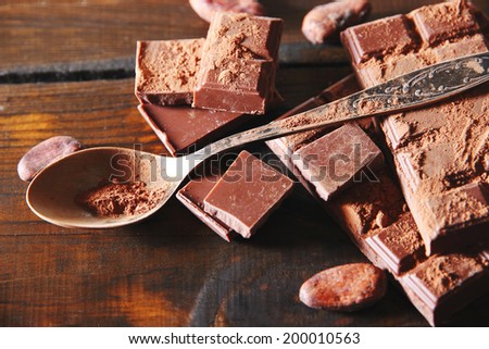 Cocoa powder and dark chocolate on color wooden background