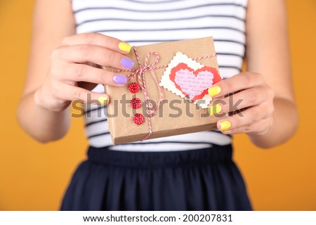 Woman with stylish colorful nails holding gift box, close-up, on color background