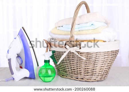 Colorful towels in basket, iron on light background