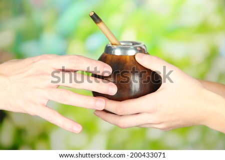 Woman hands giving calabash and bombilla with yerba mate, on nature background