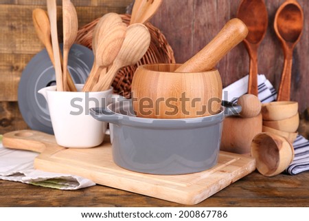 Composition of wooden cutlery, pan, bowl and cutting board on wooden background