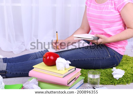 Closeup of young female student sitting on floor and studying, on light background