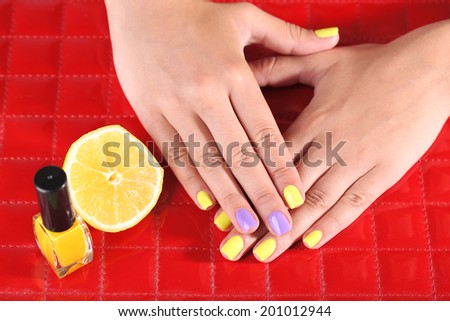 Female hand with stylish colorful nails holding fresh lemon, on color background