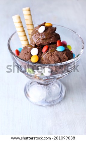Chocolate ice cream with multicolor candies and wafer rolls in glass bowl, on color wooden background