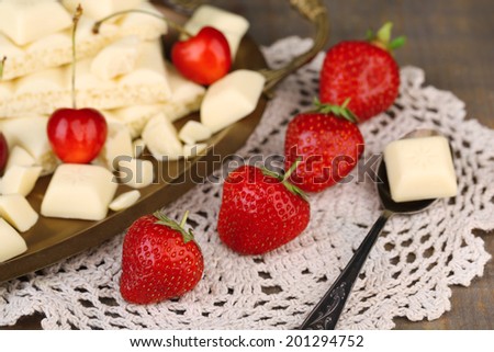 Broken white chocolate bar on tray with fresh berries, on color wooden background