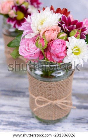 Beautiful bouquet of bright flowers in jars on table on grey background
