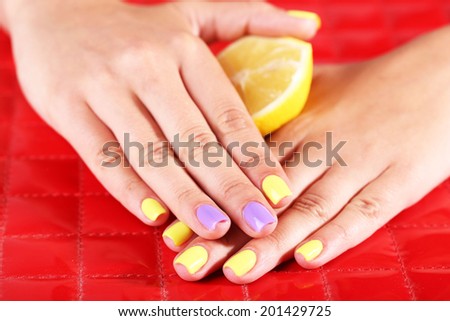 Female hand with stylish colorful nails holding fresh lemon, on color background