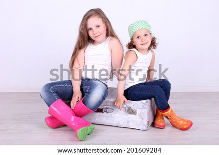 Beautiful small girls sitting on suitcase on wall background