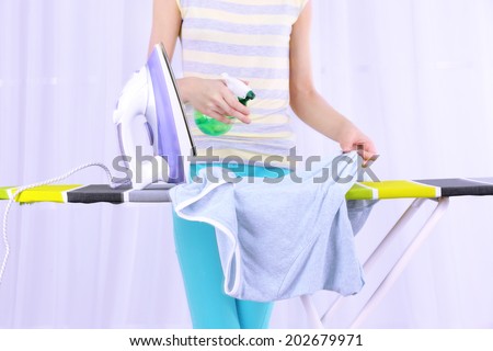 Woman ironing clothes on ironing board, close-up, on light background