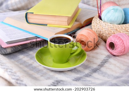 Cup of coffee and yarn for knitting on plaid with books close-up
